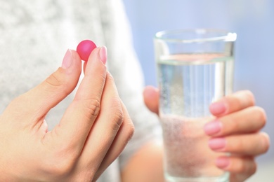 Woman holding pill and glass of water on blurred background, closeup. Space for text