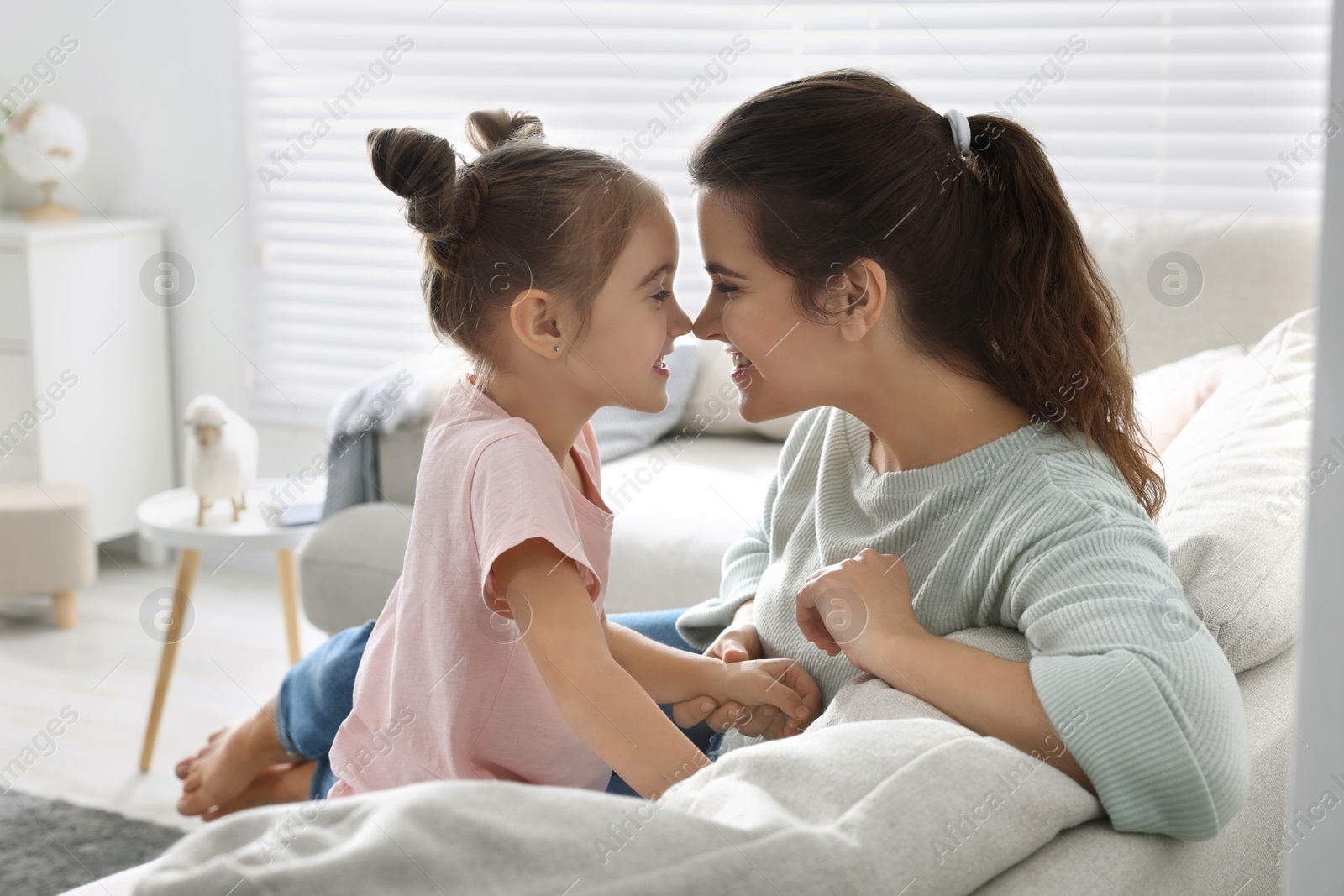 Photo of Young mother and her daughter spending time together on sofa at home