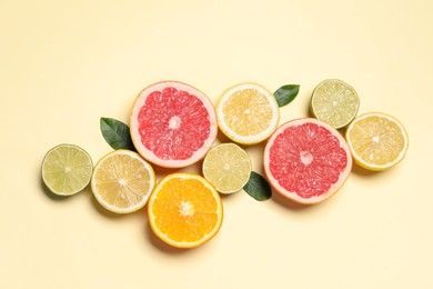 Photo of Different cut citrus fruits and leaves on beige table, flat lay