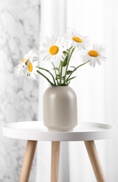 Photo of Beautiful tender chamomile flowers in vase on white table indoors