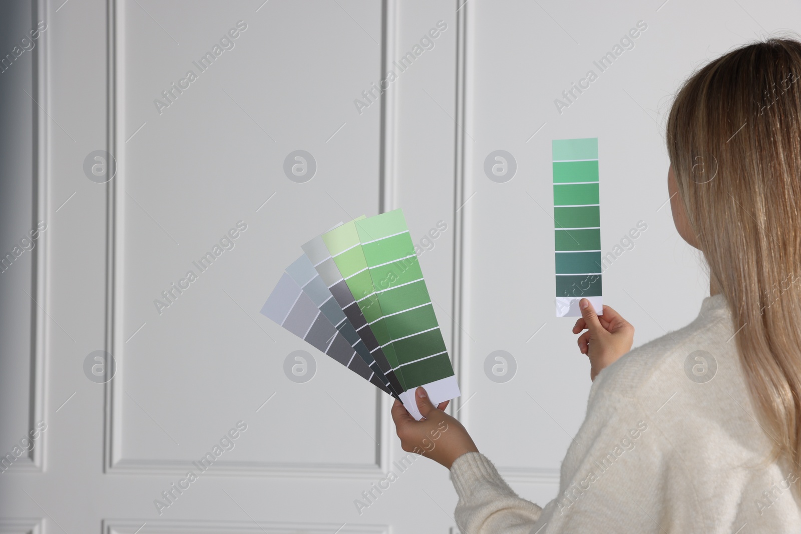 Photo of Woman choosing color for wall indoors, focus on hands with paint chips. Interior design