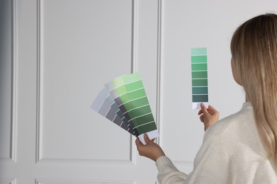 Woman choosing color for wall indoors, focus on hands with paint chips. Interior design