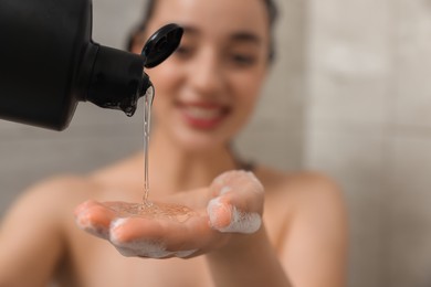 Washing hair. Happy woman pouring shampoo into hand in shower, selective focus. Space for text