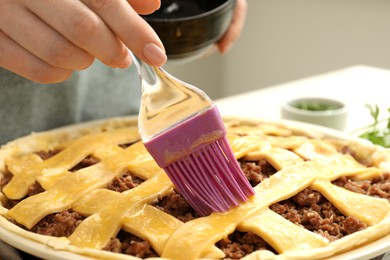 Woman spreading egg yolk onto raw meat pie, closeup