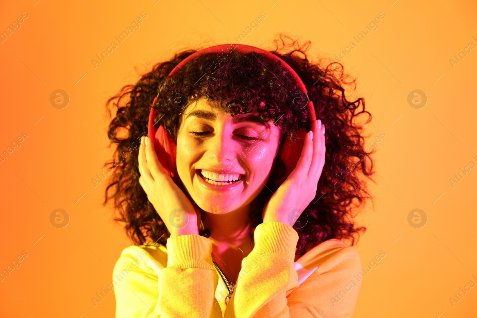 Photo of Beautiful young woman listening to music with headphones on color background in neon lights