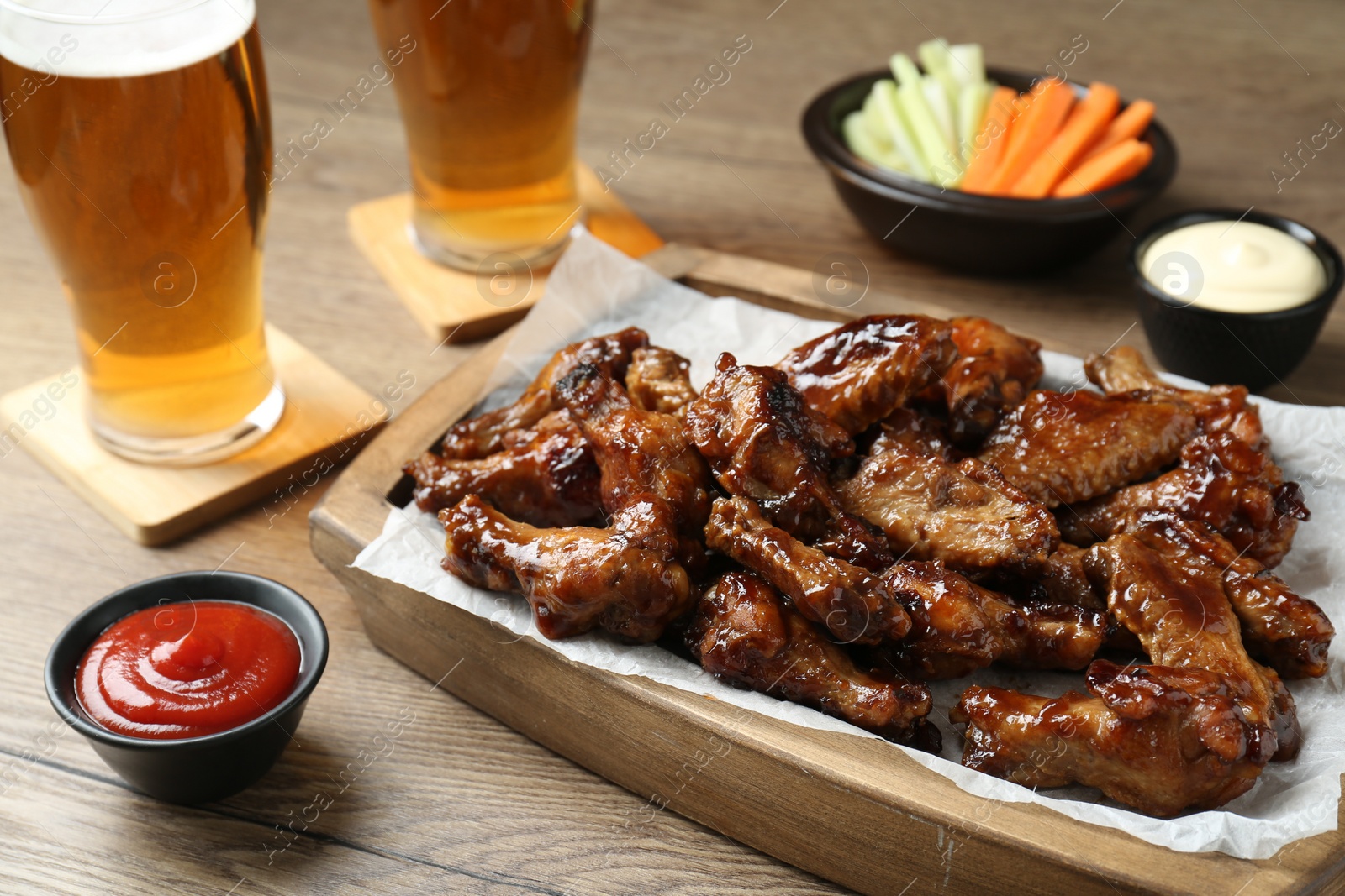 Photo of Tasty chicken wings, sauces, vegetable sticks and glasses of beer on wooden table, closeup. Delicious snacks