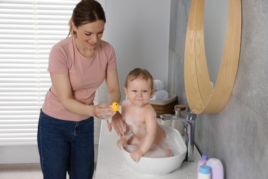 Mother washing her little baby in sink at home