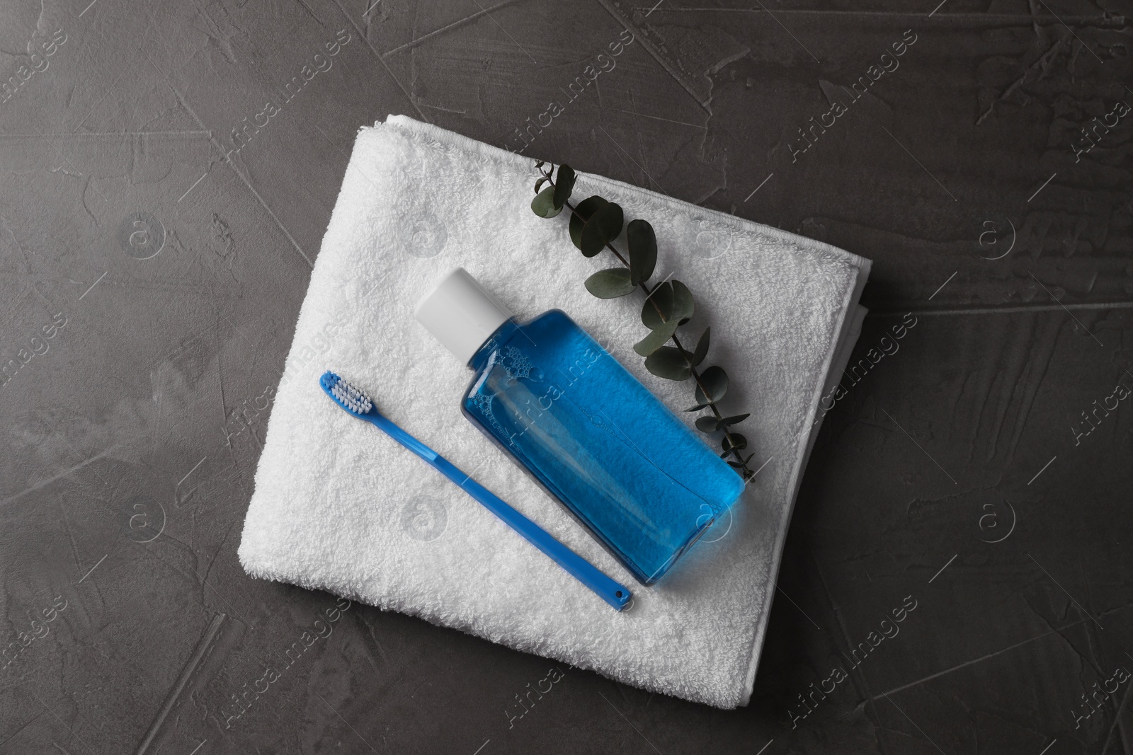 Photo of Fresh mouthwash in bottle, toothbrush, eucalyptus branch and towel on dark textured table, top view