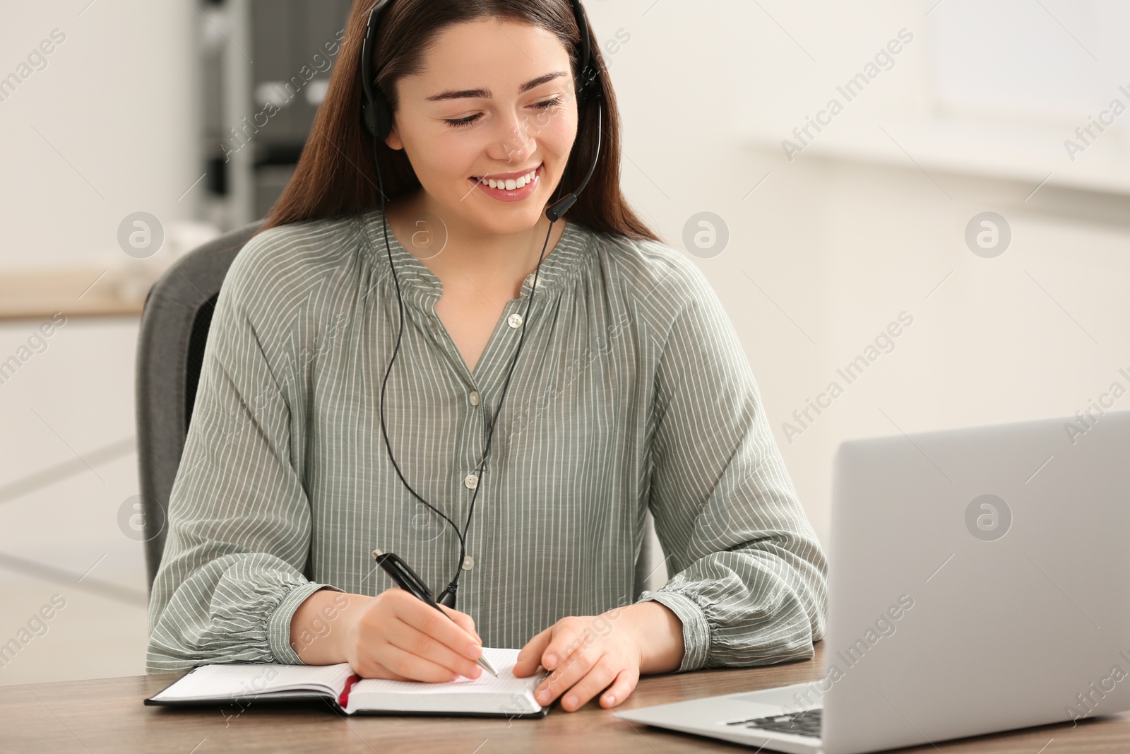 Photo of Hotline operator with headset and notebook working in office