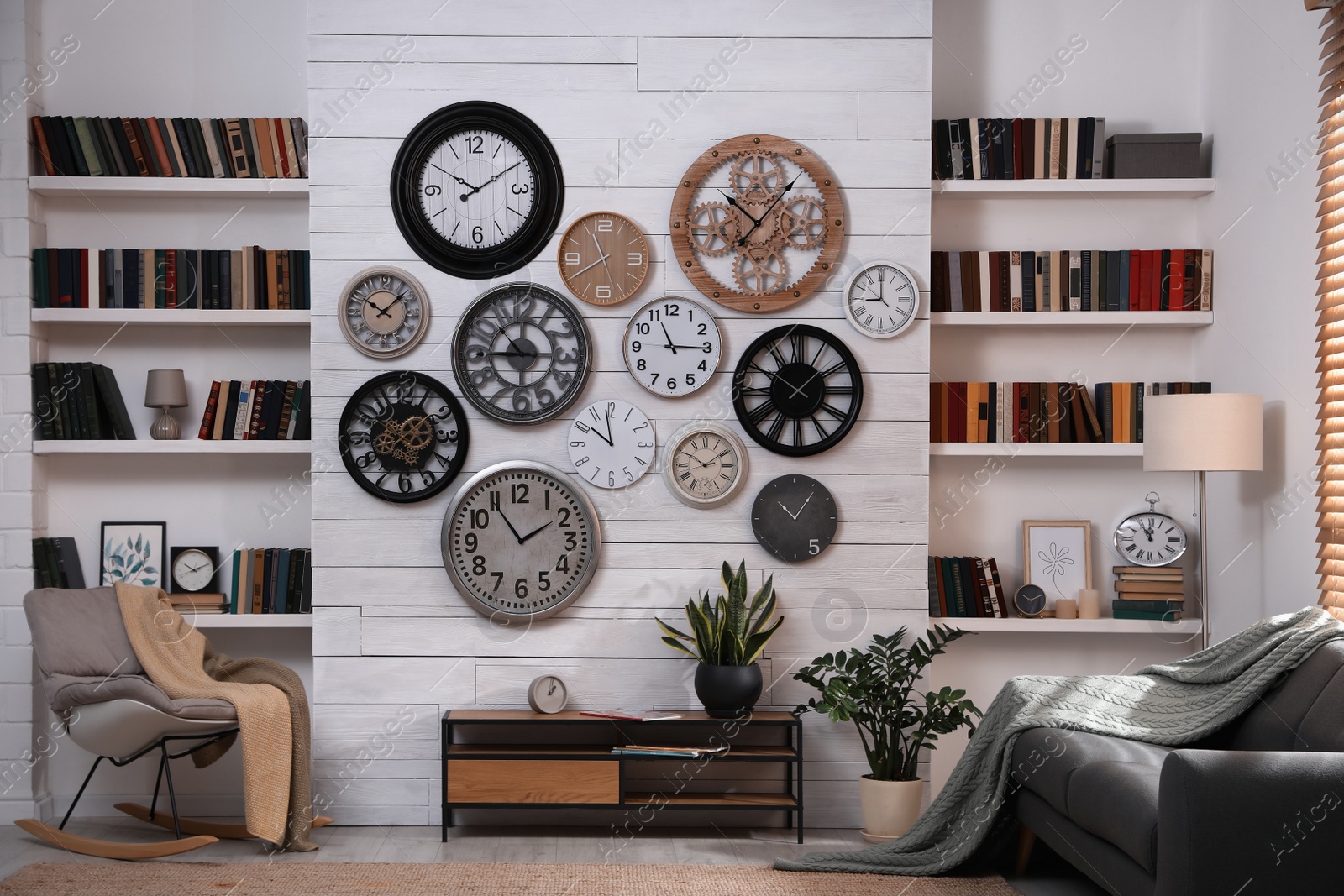 Photo of Stylish room interior with console table, comfortable furniture and collection of different clocks on white wall