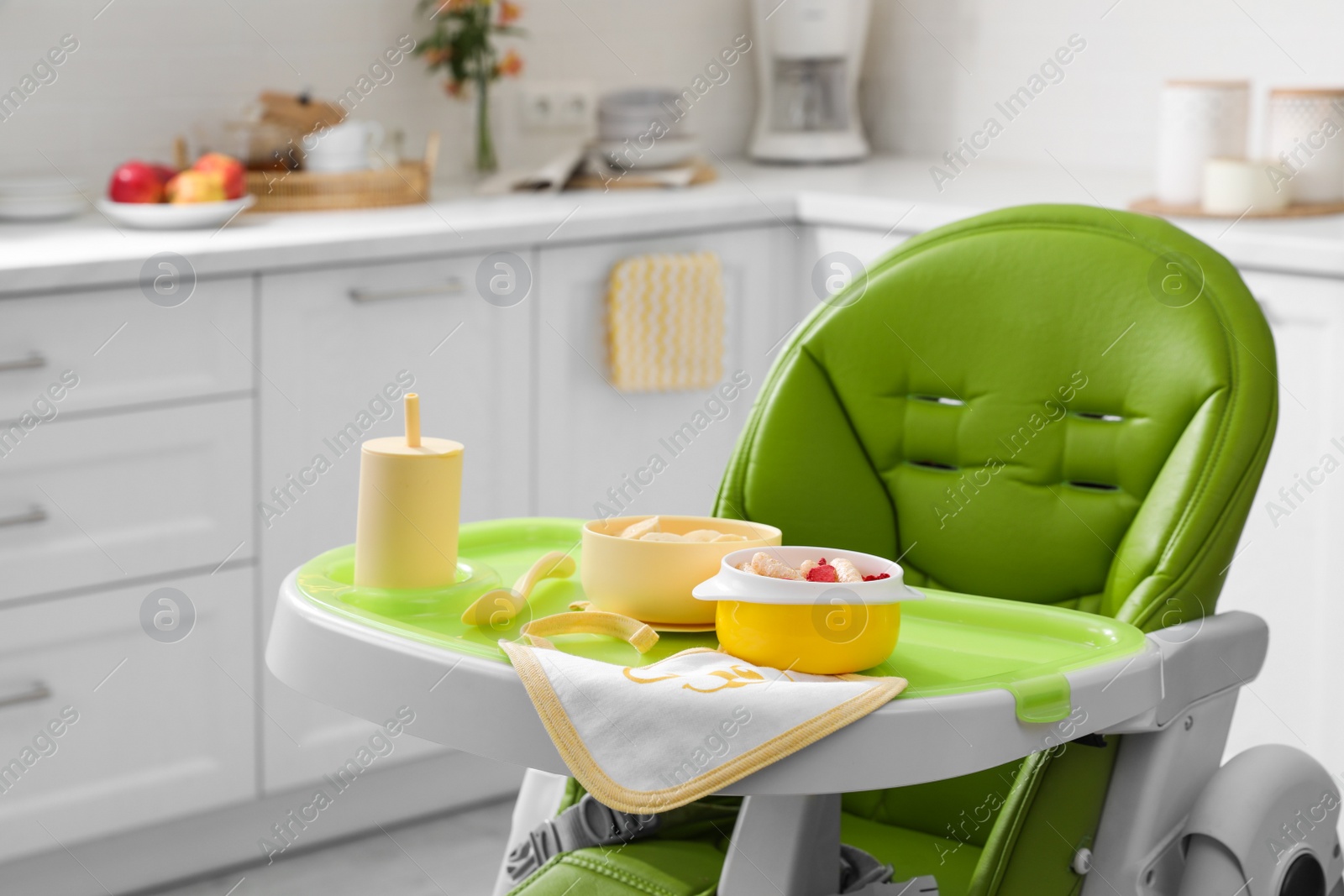 Photo of High chair with food in baby tableware on tray indoors