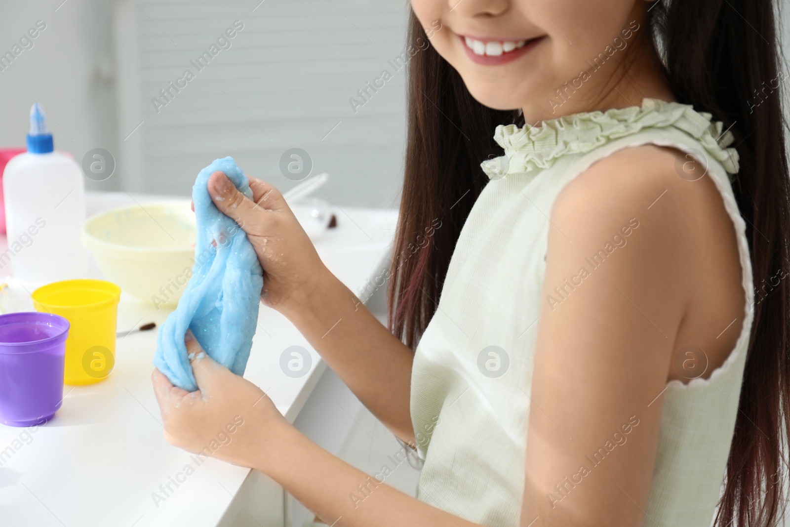 Photo of Little girl making DIY slime toy at table in room, closeup