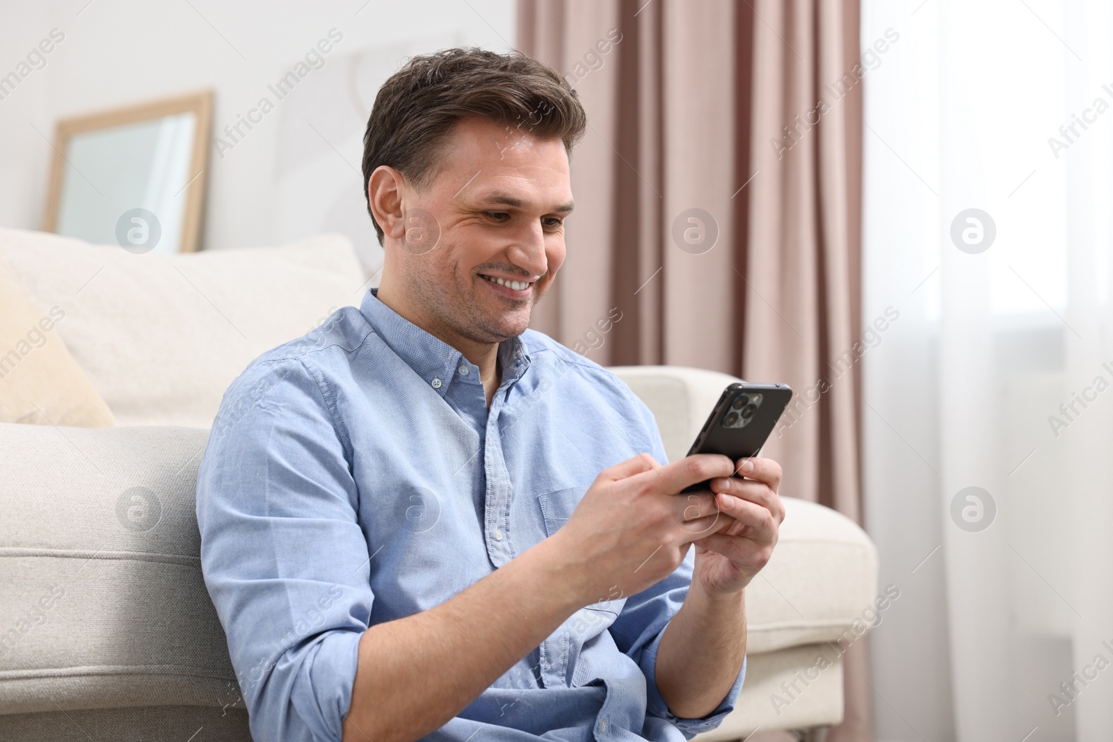 Photo of Handsome happy man using smartphone at home