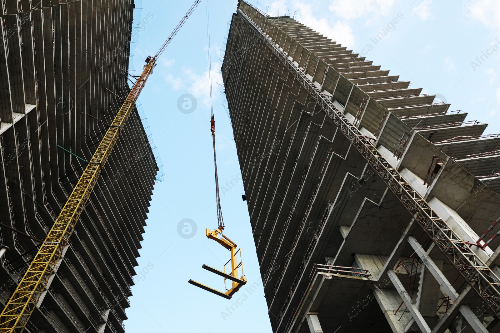 Photo of Tower crane near unfinished buildings against cloudy sky on construction site, low angle view