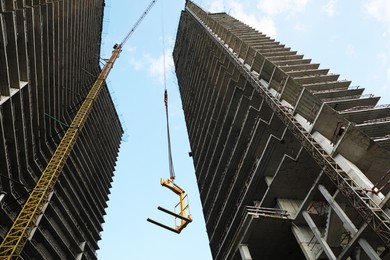 Tower crane near unfinished buildings against cloudy sky on construction site, low angle view