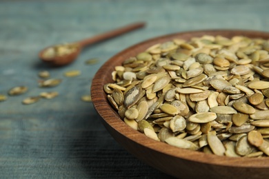 Photo of Bowl of raw pumpkin seeds on blue wooden table, closeup. Space for text