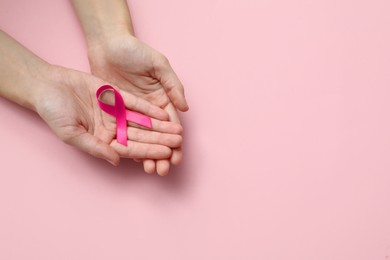 Woman holding pink ribbon on color background, top view with space for text. Breast cancer awareness concept