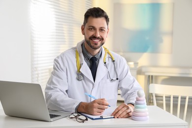 Pediatrician with stethoscope at table in clinic