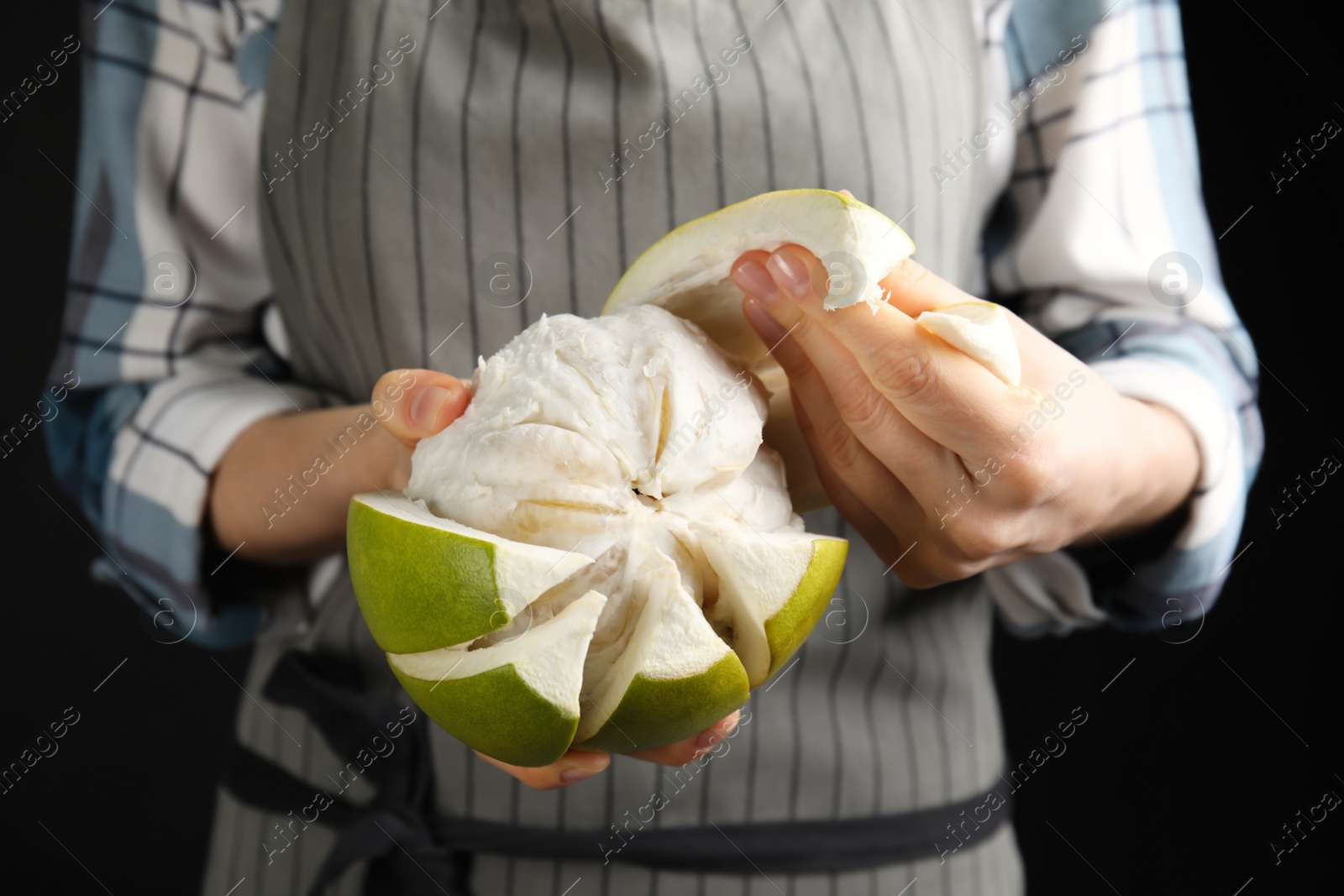 Photo of Woman peeling fresh ripe pomelo on black background, closeup