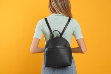 Photo of Woman with stylish backpack on yellow background, back view