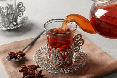 Photo of Pouring traditional Turkish tea from pot into glass on table, closeup