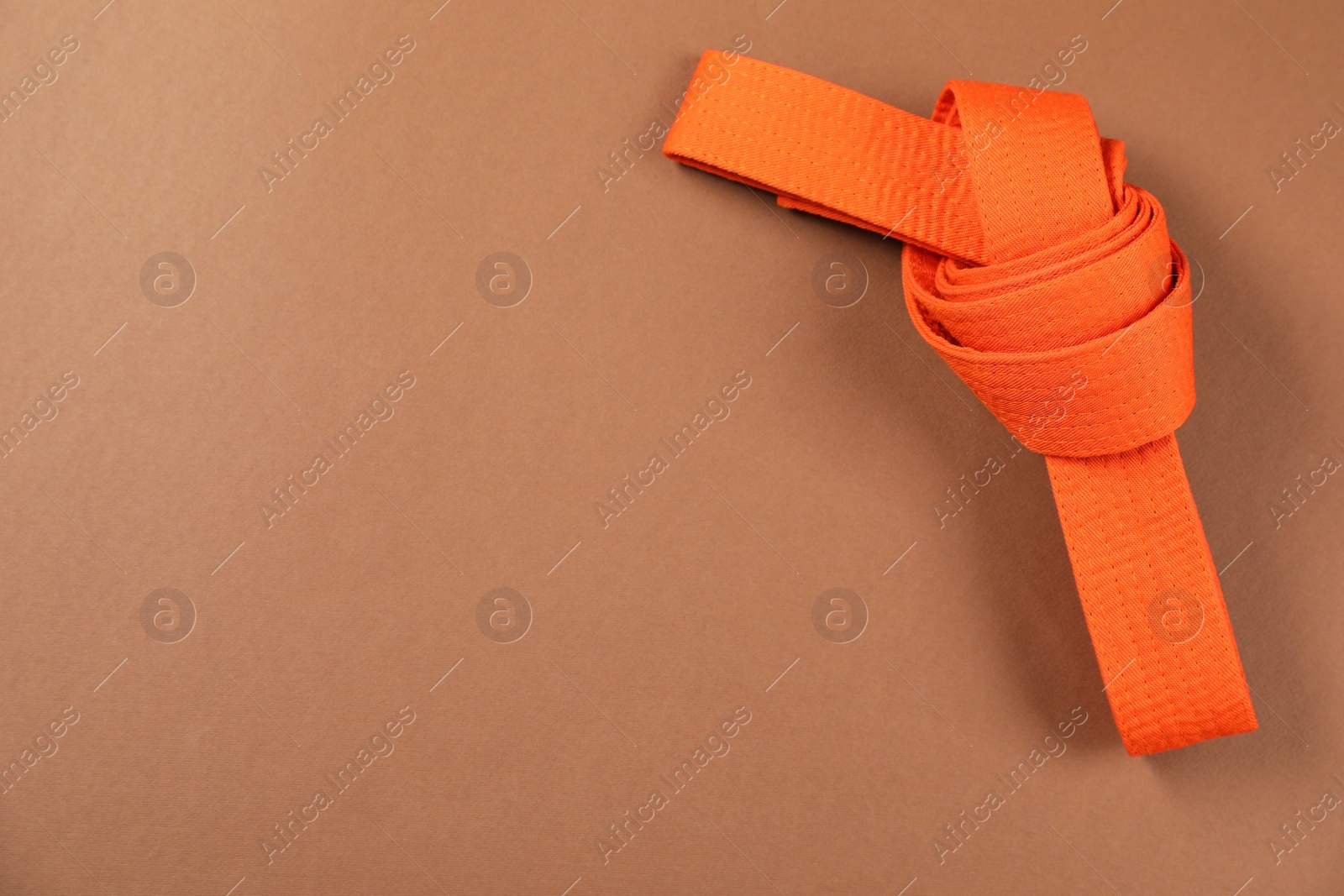 Photo of Orange karate belt on brown background, top view. Space for text