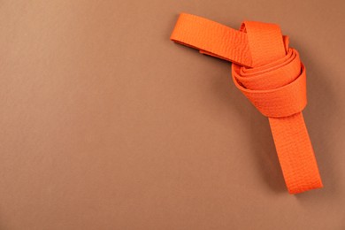 Photo of Orange karate belt on brown background, top view. Space for text