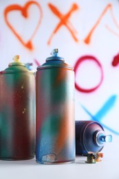 Many spray paint cans near white wall with different drawn symbols