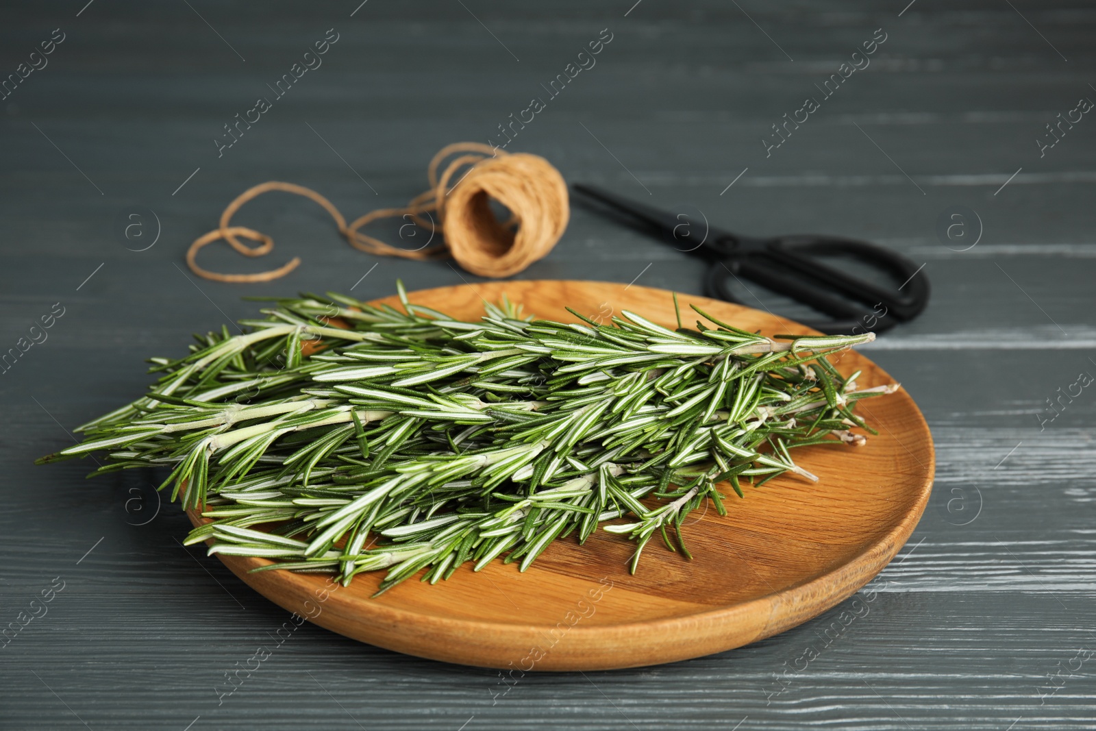 Photo of Wooden plate with fresh rosemary twigs, scissors and twine on table