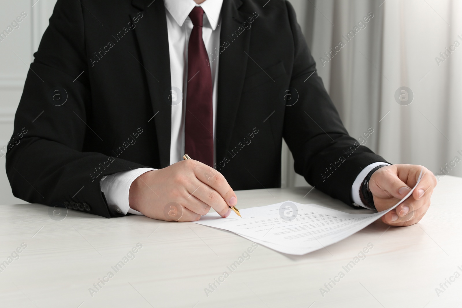 Photo of Notary signing document at wooden table indoors, closeup