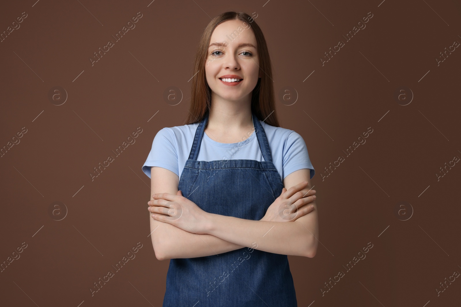 Photo of Beautiful young woman wearing kitchen apron on brown background. Mockup for design