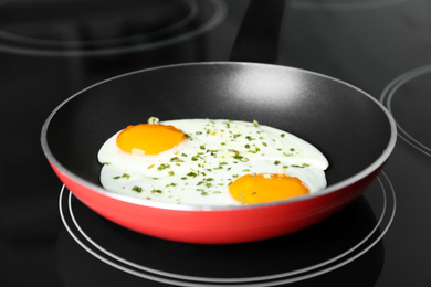 Photo of Chicken eggs with herbs in frying pan on stove, closeup