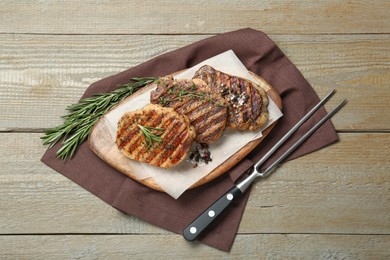 Photo of Delicious grilled pork steaks with herbs, spices and carving fork on wooden table, top view
