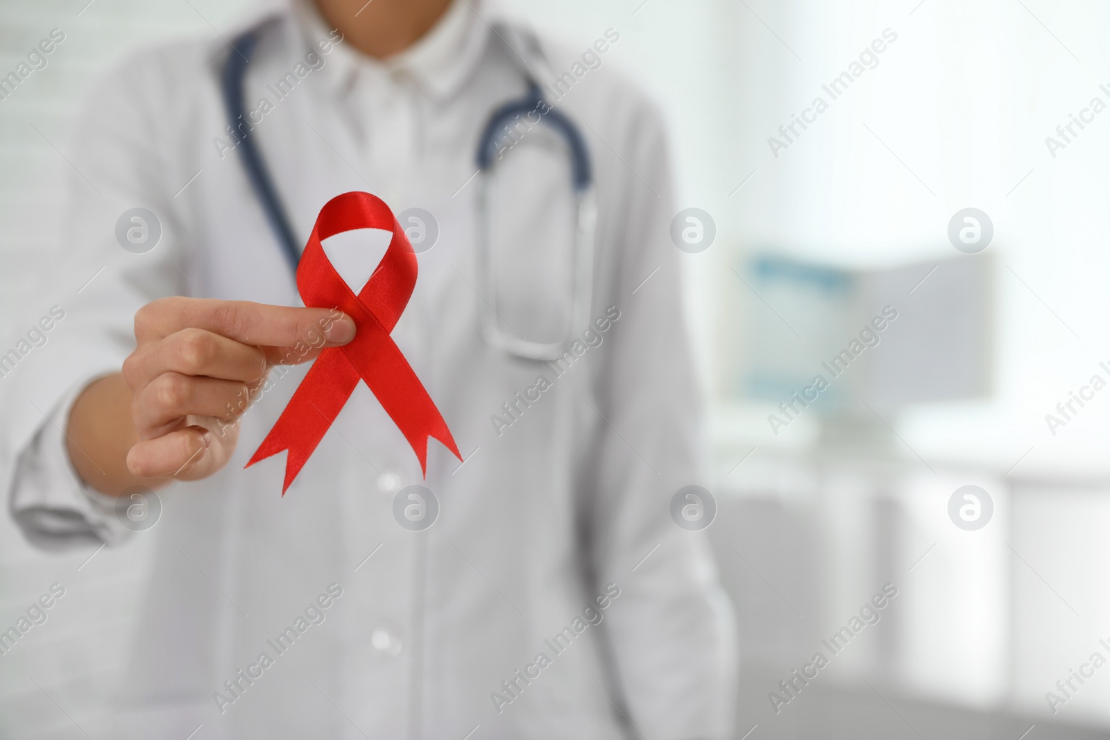 Photo of Doctor holding red ribbon on blurred background, closeup with space for text. AIDS awareness month