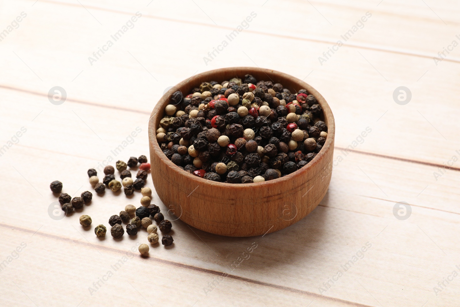 Photo of Aromatic spices. Different peppers in bowl on wooden table