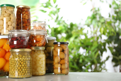 Photo of Glass jars of different pickled vegetables on marble table. Space for text