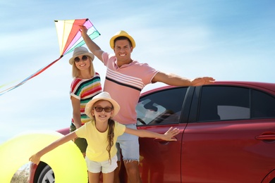 Photo of Happy family with inflatable ring and kite near car outdoors. Trip to beach