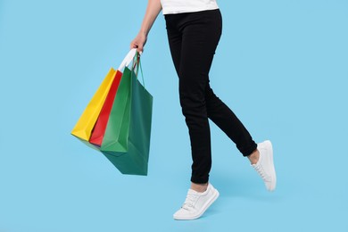 Woman with shopping bags on light blue background, closeup