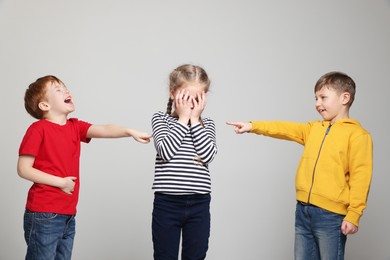 Photo of Boys pointing at upset girl on light grey background. Children's bullying