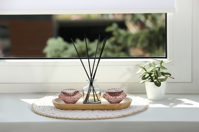 Reed diffuser with burning candles and houseplant on white window sill