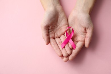 Woman holding pink ribbon on color background, top view with space for text. Breast cancer awareness concept