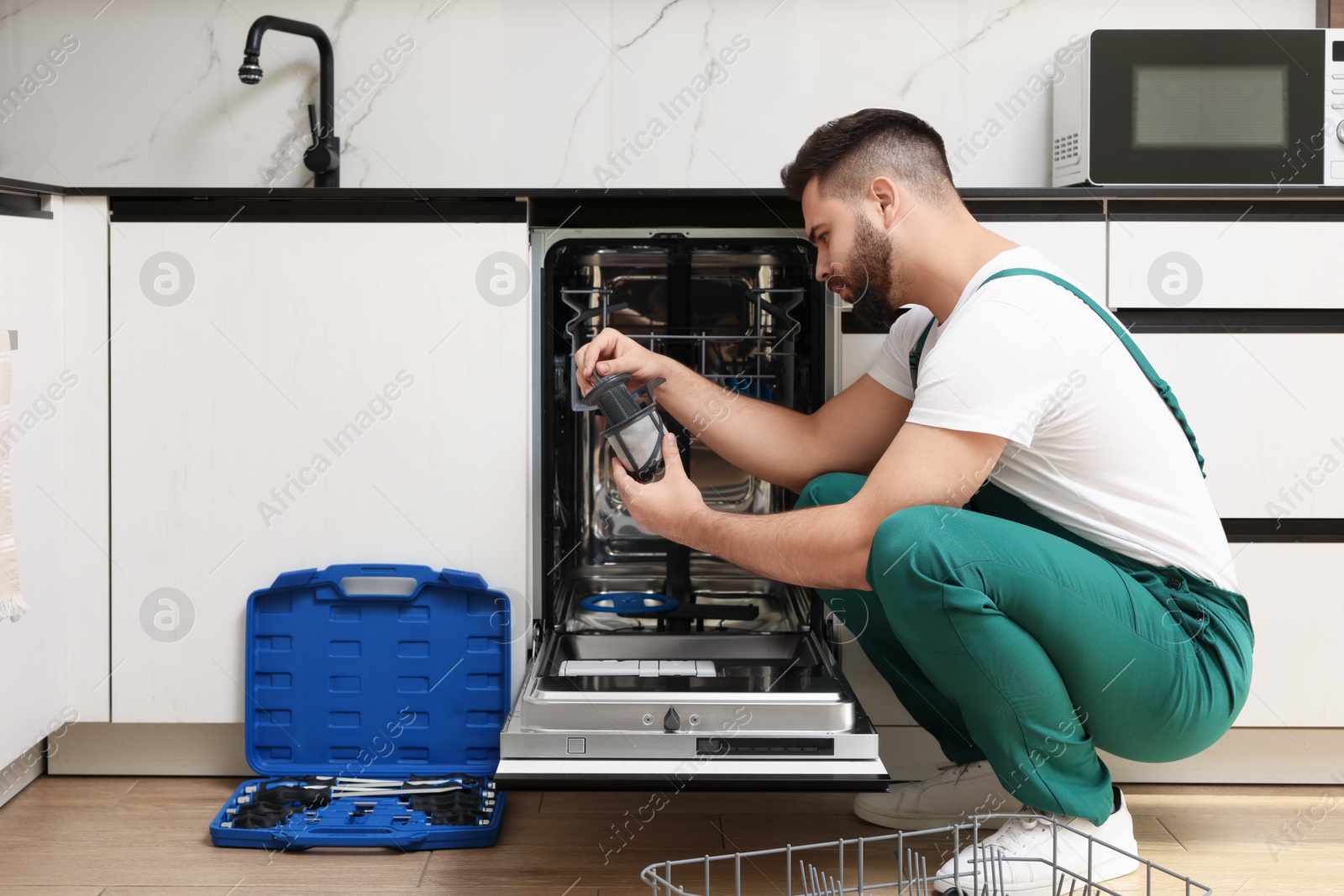 Photo of Repairman holding drain filter near dishwasher in kitchen