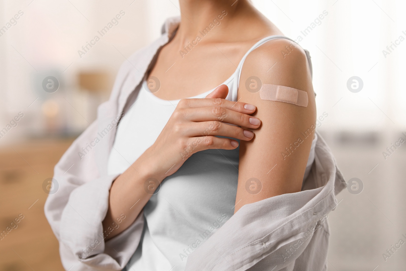 Photo of Woman with sticking plaster on arm after vaccination at home, closeup