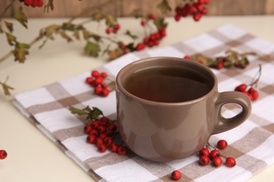 Brown cup with hawthorn tea and berries on beige table