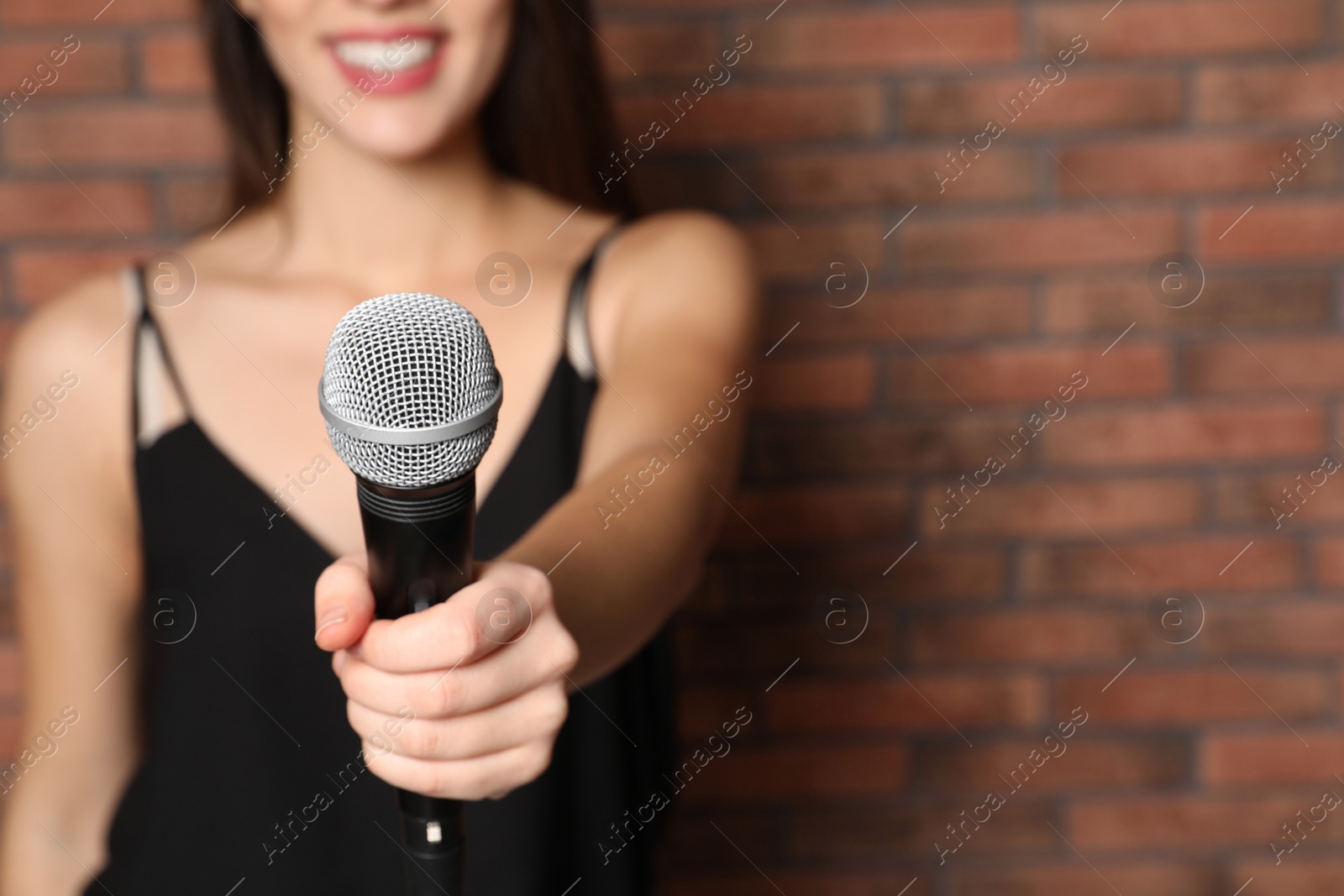 Photo of Young woman holding microphone near brick wall, closeup view with space for text