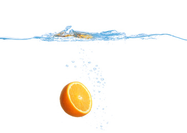 Ripe orange falling down into clear water against white background