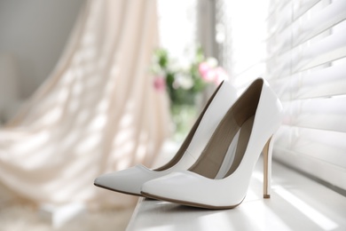 Pair of white high heel shoes and blurred wedding dress on background, space for text