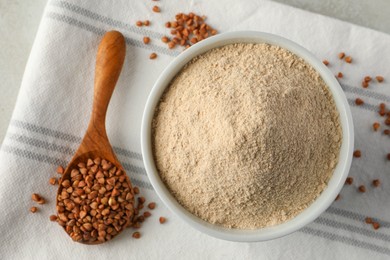 Photo of Bowl of flour and spoon with buckwheat on cloth, flat lay