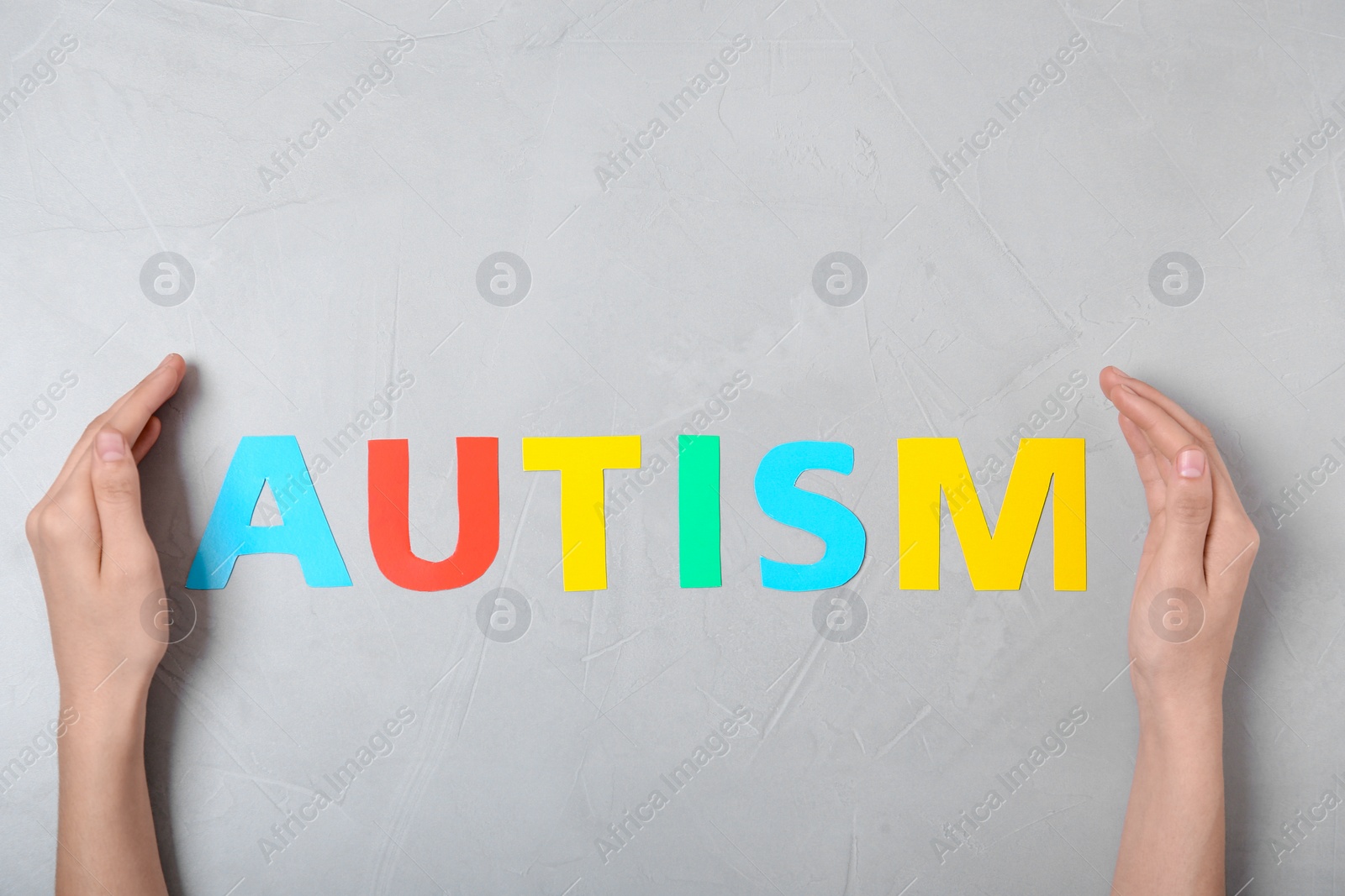 Photo of Female hands and word AUTISM on grey background, top view