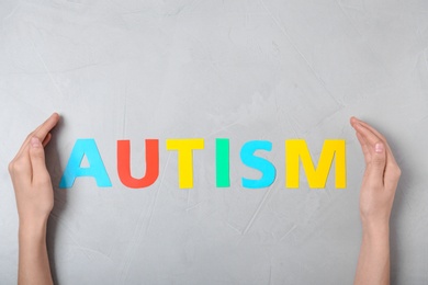 Photo of Female hands and word AUTISM on grey background, top view